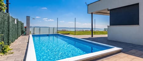 A rectangular swimming pool with a clear blue water surface, surrounded by a paved deck.