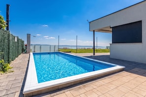 Una piscina rectangular con superficie de agua azul cristalina, rodeada por una terraza empavedada.