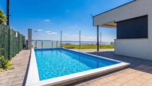 A rectangular swimming pool with a clear blue water surface, surrounded by a paved deck. - Lelle Marine-hanna Pool Apartment (Balatonlelle)