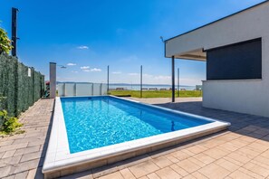Una piscina rectangular con superficie de agua azul cristalina, rodeada por una terraza empavedada.