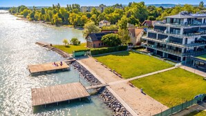 A riverside property with a wooden dock, a grassy lawn, and a modern building with balconies. - Lelle Marine-hanna Pool Apartment (Balatonlelle)