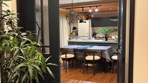 A modern kitchen with a dining area, wooden flooring, and a large potted plant.