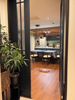 A modern kitchen with a dining area, wooden flooring, and a large potted plant.