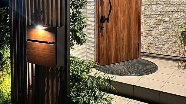 A modern entrance with a wooden door, a vertical wooden panel, and a stone-textured wall.