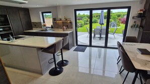 Una cocina moderna con una isla grande, un comedor con mesa y sillas, y un ventanal corredero que da a un jardín.