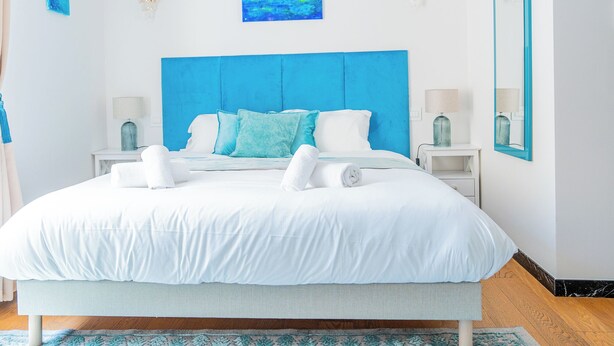 Une chambre à coucher moderne avec un grand lit, une literie blanche, une tête de lit bleue et un tableau au-dessus du lit.