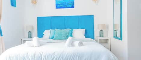 Ein modernes Schlafzimmer mit einem großen Bett, weißer Bettwäsche, einem blauen Kopfteil und einem Bild darüber.