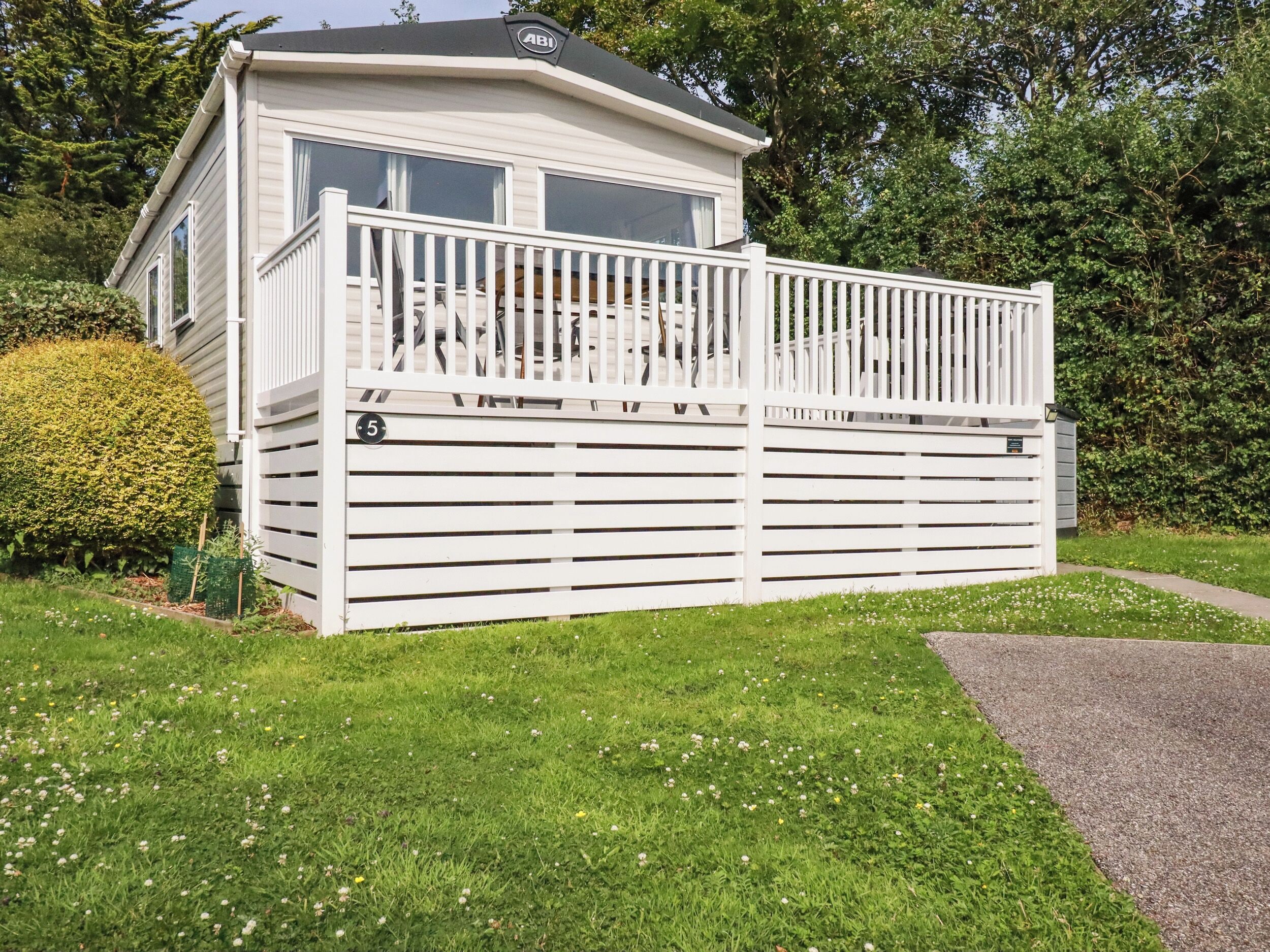 A single-story mobile home with a balcony, a number '5' sign, and a well-maintained lawn.