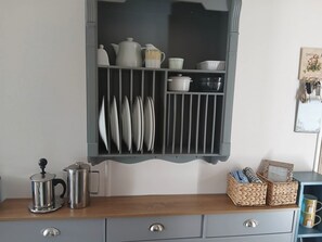 A kitchen with a built-in shelf holding various kitchenware, a coffee maker, and woven baskets on a wooden countertop. - Porthcurno 5 (Truro)