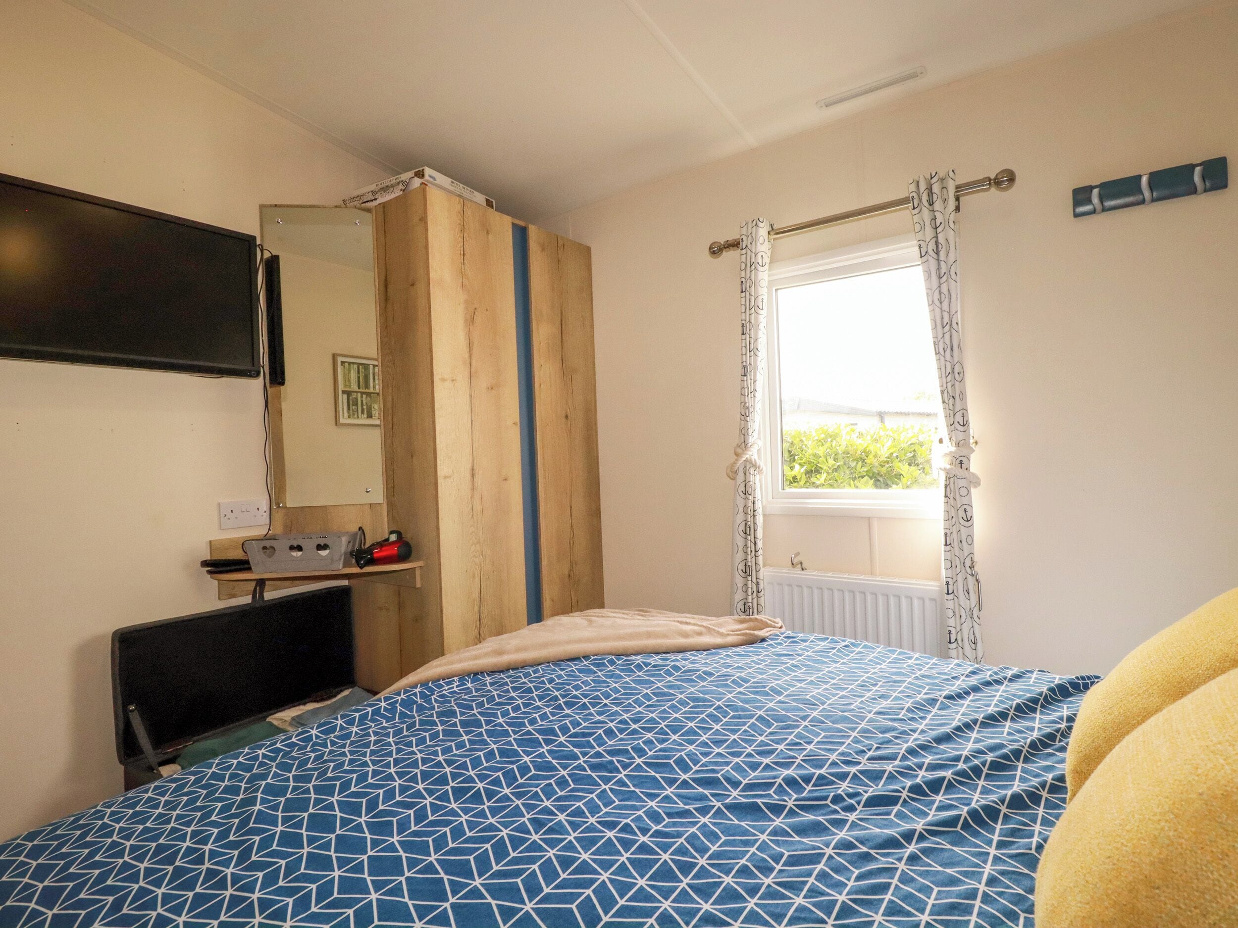 A bedroom with a bed, a TV, a wooden wardrobe, a window with curtains, and a radiator.