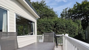 Eine überdachte Terrasse im Freien mit Tisch und Stühlen, weißen Geländern und Blick auf Bäume.