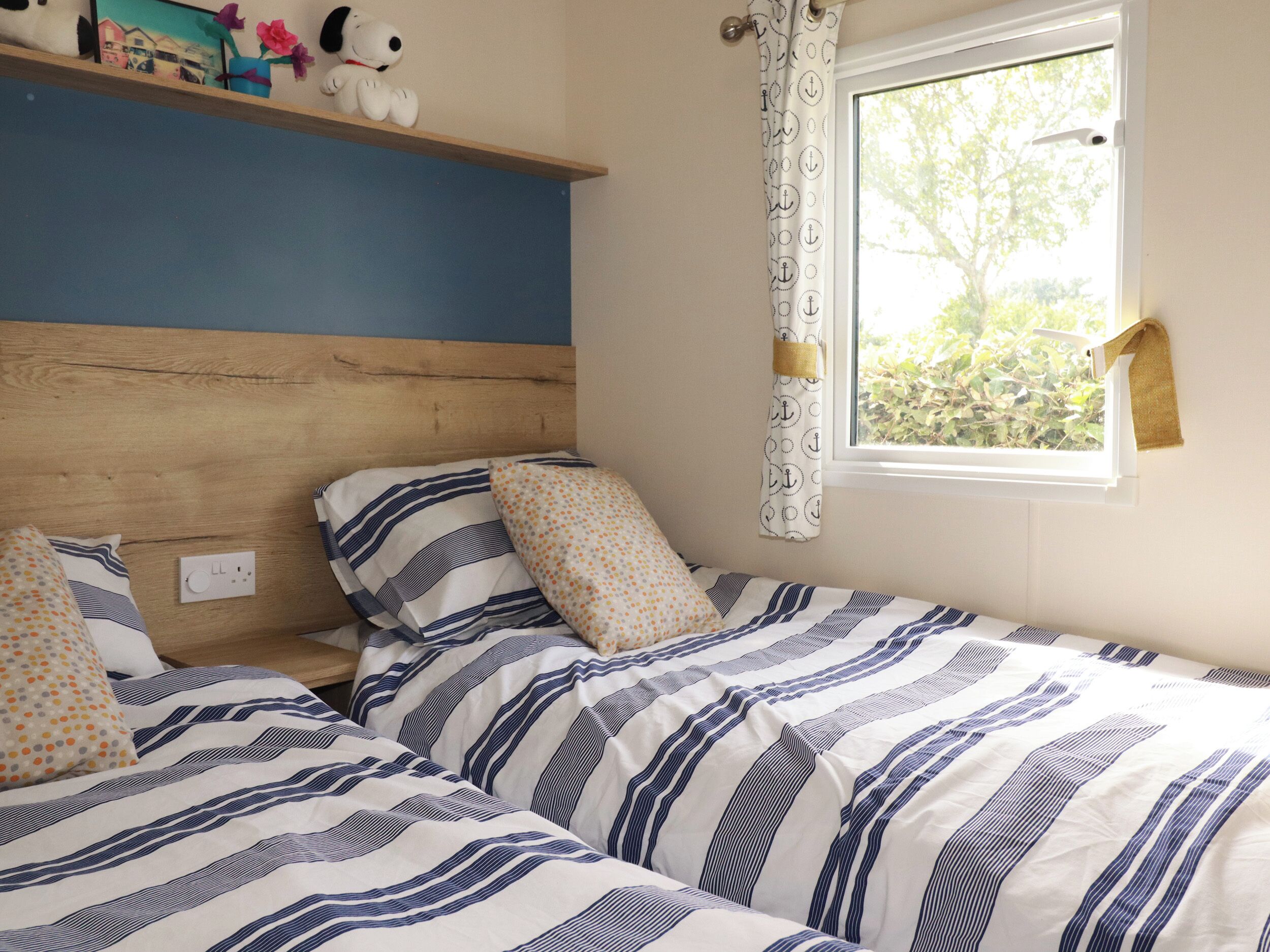 Une chambre avec deux lits, une tête de lit en bois, une fenêtre avec des rideaux et une étagère ornée d’objets décoratifs.