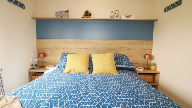 Ein Schlafzimmer mit blau gemustertem Bettbezug, Holz-Kopfteil, zwei Nachttischen mit Lampen und Dekorationen auf dem Nachttisch.