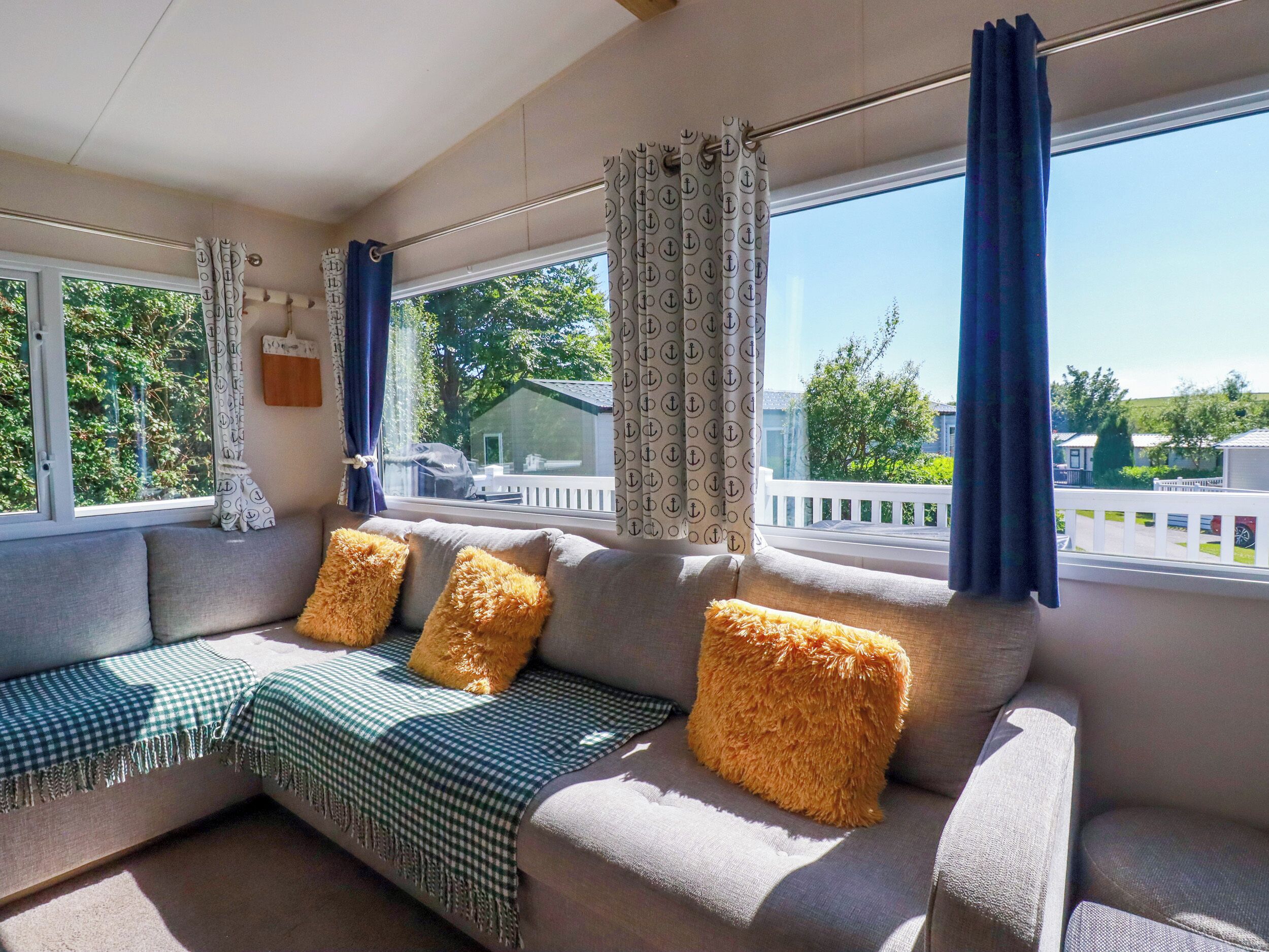A cozy living room with a sofa, patterned curtains, and a view of a white fence and greenery outside.