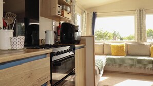 Eine Küche mit Herd, Backofen und diversen Küchenutensilien. Ein Sofa mit Kissen und Blick auf Bäume draußen.