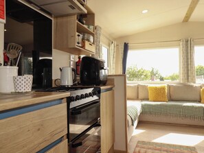 Eine Küche mit Herd, Backofen und diversen Küchenutensilien. Ein Sofa mit Kissen und Blick auf Bäume draußen.