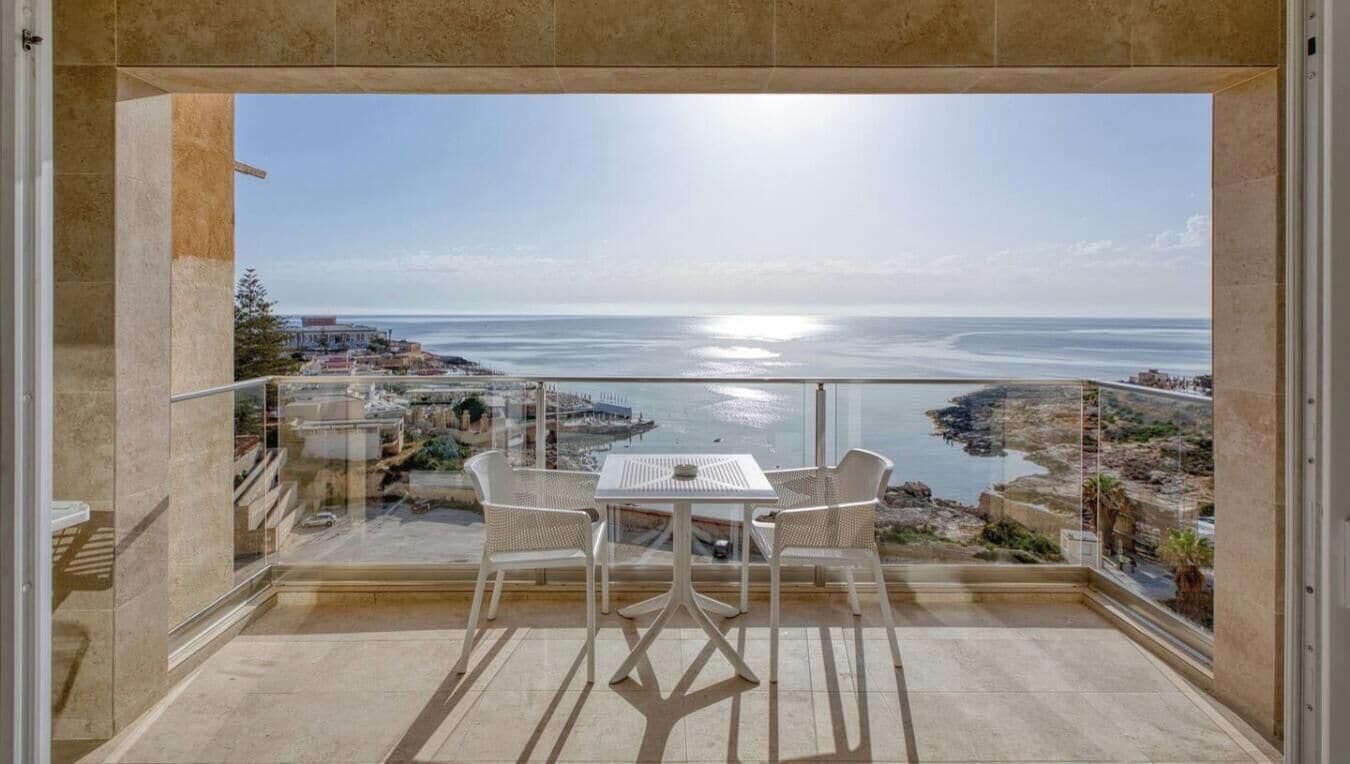 A balcony with a view of the sea, a table, and two chairs.