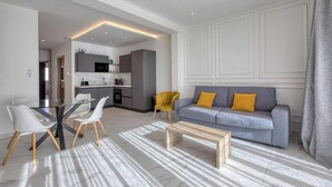 Uma sala de estar moderna com uma mesa de jantar de vidro, um sofá cinza com almofadas amarelas e uma mesa de centro de madeira.
