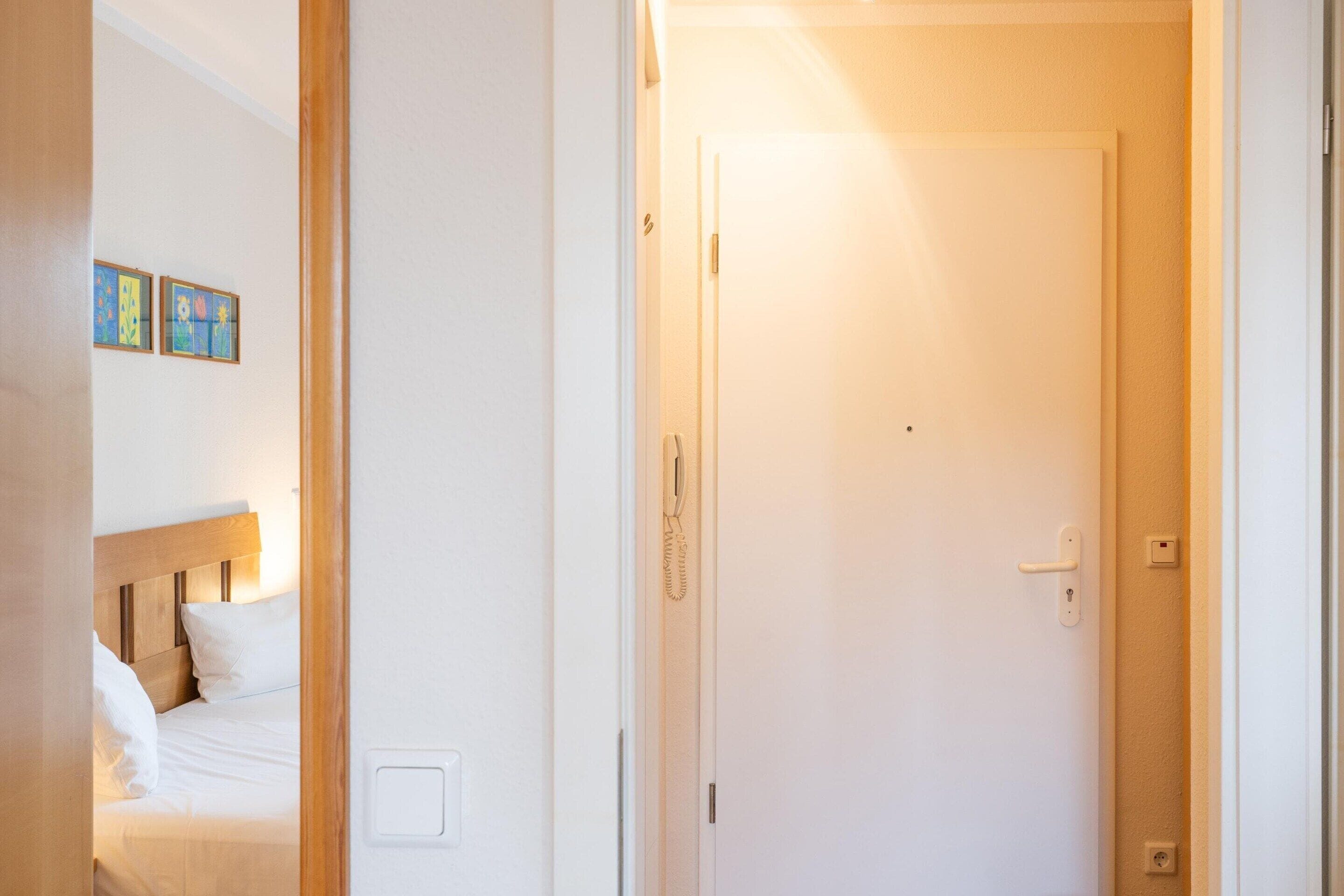 A hotel room with a bed, a door, and a wall-mounted light switch.