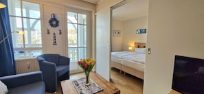 A room with a bed, a chair, a table with a vase of flowers, and a TV. - Moderne Ferienwohnung mit Balkon Strandnah im Seepark Sellin (Sellin)