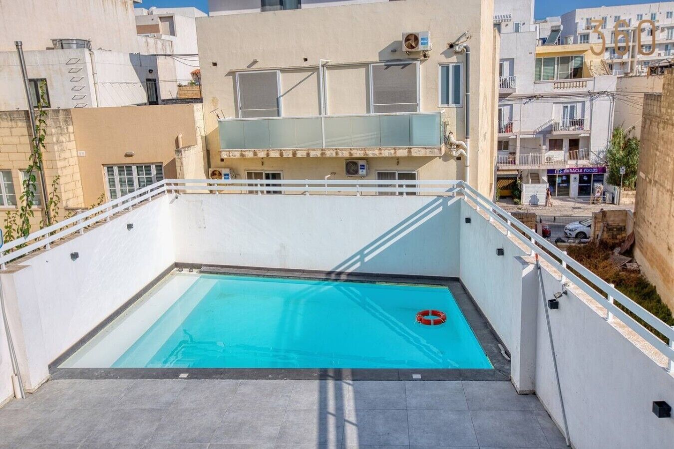 Una piscina en la azotea con un flotador salvavidas, rodeada de edificios.