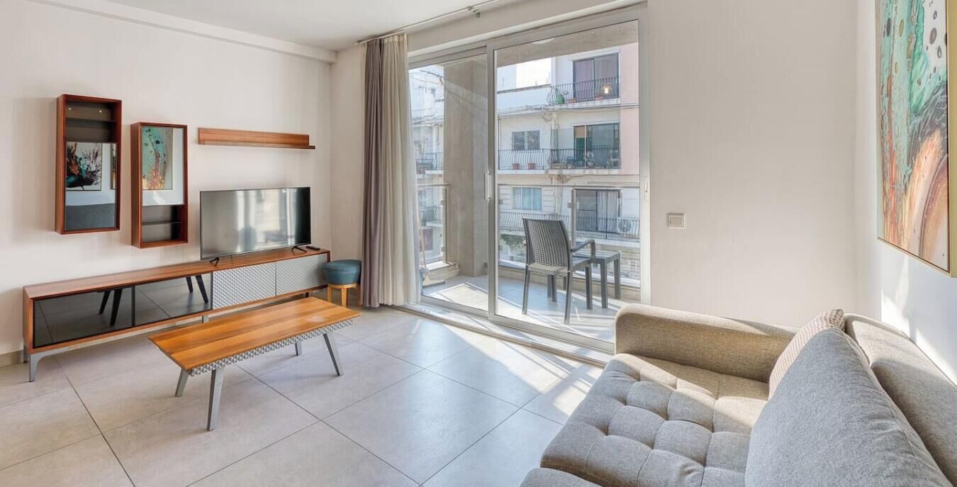 A modern living room with a sofa, a wooden coffee table, a TV, and artwork on the wall.