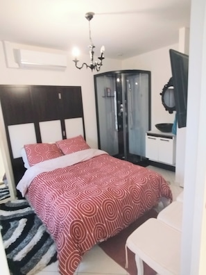 Une chambre à coucher avec un lit, un lustre, une armoire et une salle de bain dotée d’une porte en verre.