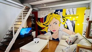 Un salon moderne avec un escalier, un canapé, une table basse et une fresque murale.