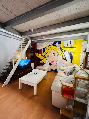 A modern living room with a staircase, a sofa, a coffee table, and a mural. - Stay in this pleasant and cozy, pet-friendly loft-style apartment in the city center (Vallecas)