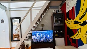 Un salon avec un téléviseur diffusant une vue sur la ville, un verre de bière, un canapé et un escalier.