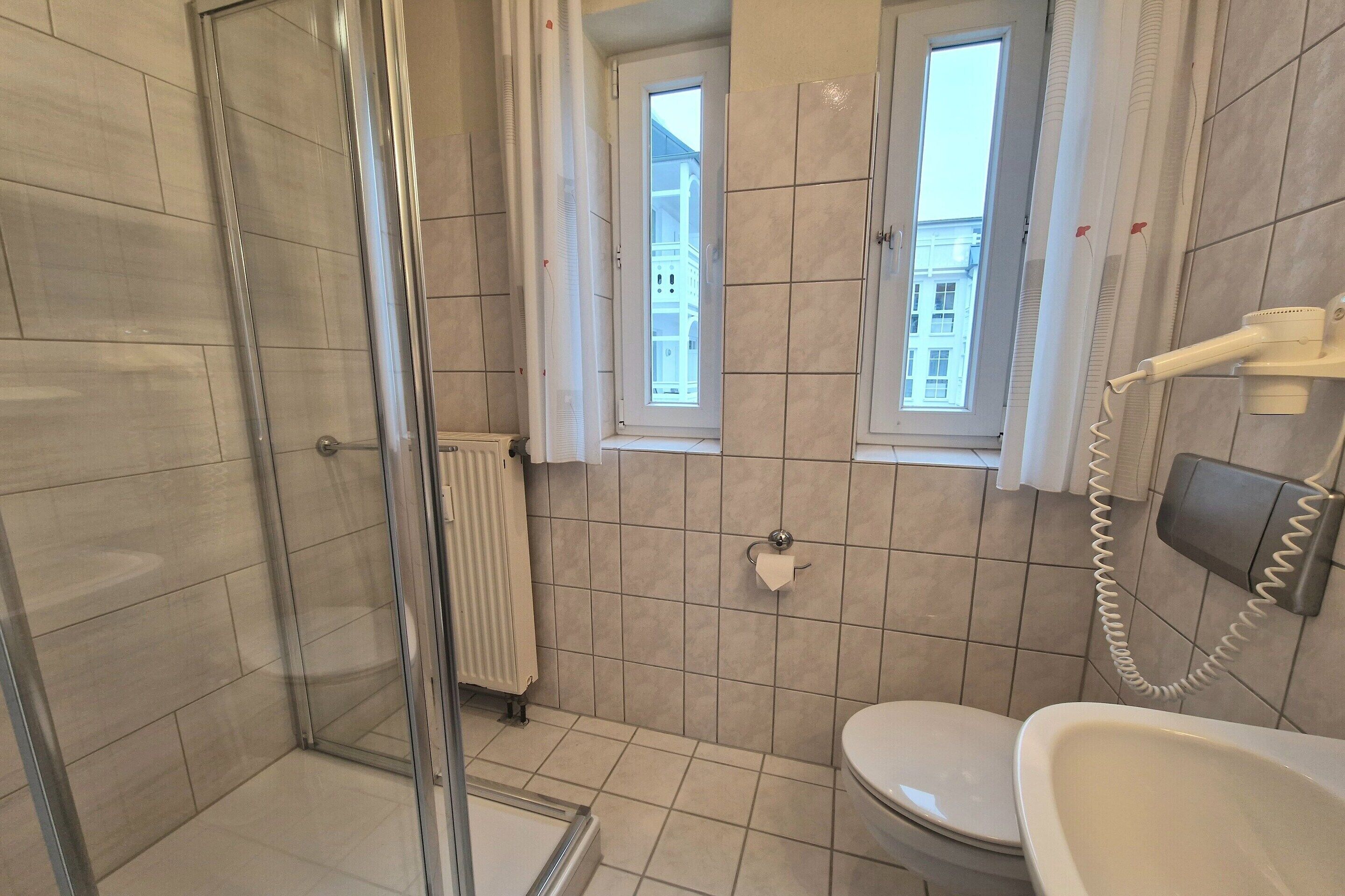 A bathroom with a glass shower enclosure, a toilet, a bidet, and a hairdryer mounted on the wall.