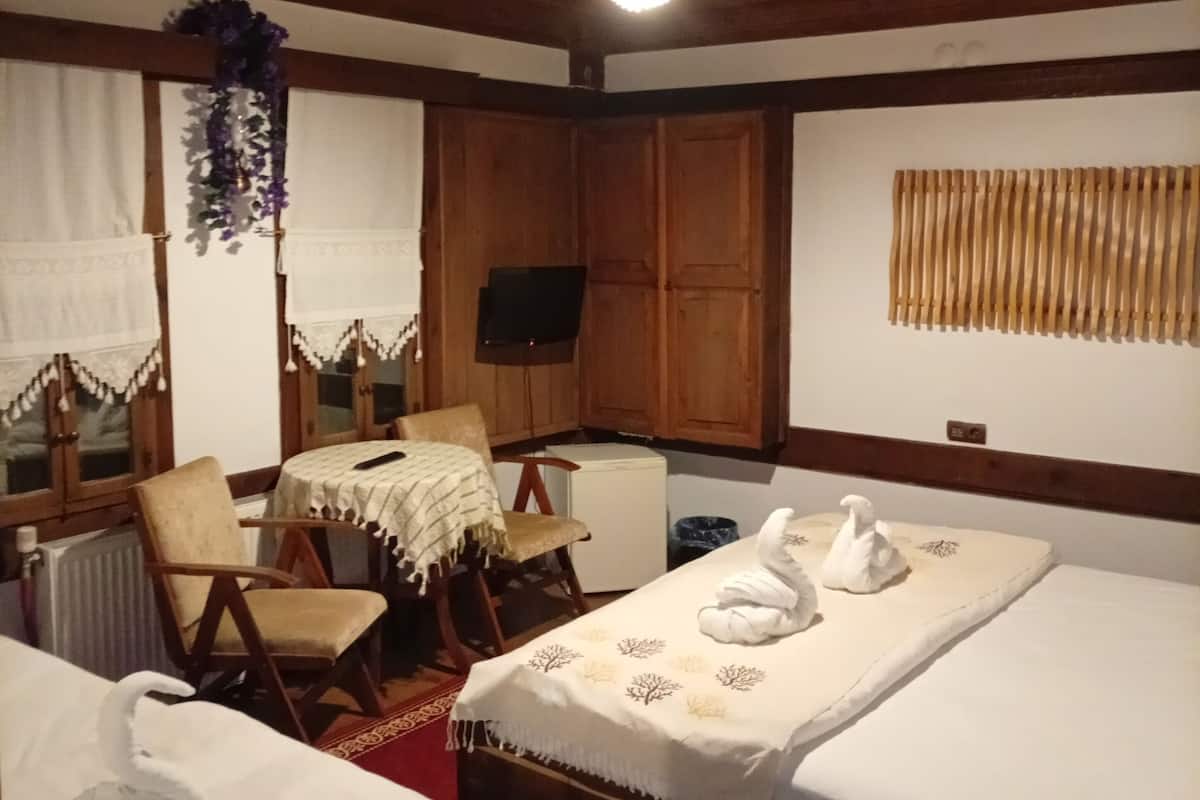 A room with wooden ceilings, a bed with a white bedspread, a chair, a table with a white tablecloth, and a television.