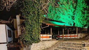 A stone-paved entrance with steps leading to a building with a green-lit roof and a covered area with striped awnings.