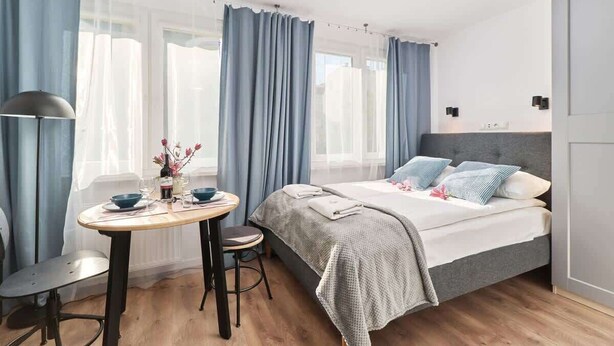 Ein modernes Schlafzimmer mit einem Bett, einem Tisch mit Stühlen und einem Fenster mit Vorhängen.