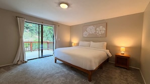 A bedroom with a large bed, a nightstand with a lamp, a ceiling light, a sliding glass door to a deck, and a floral wall art piece. - Fernan Retreat 3BR Minutes to Downtown the Lake (Coeur d'Alene)