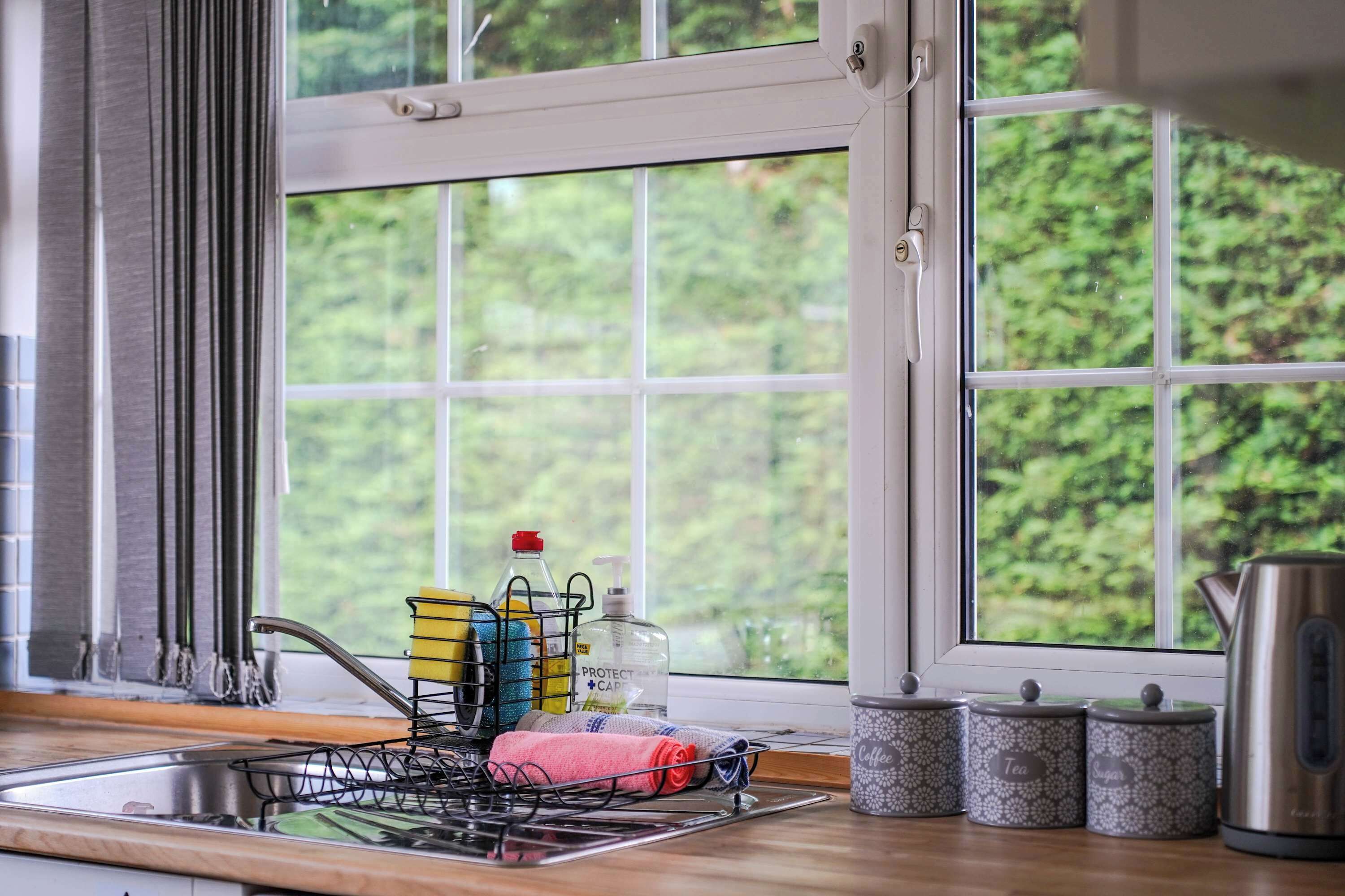 A kitchen with a window, a sink, dish rack, tea containers, and a kettle.
