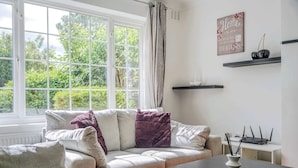 Ein Wohnzimmer mit einer Couch, einem Couchtisch, einem Fenster mit Vorhängen, einer Wandregal mit Dekoration und einem Schild mit Text.