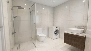 Ein modernes Badezimmer mit einer Duschkabine, Toilette, Waschmaschine und einem Waschtisch.