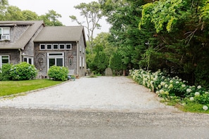 A two-story house with a gravel driveway leading to a wooden gate. - Vineyard Retreat | Artsy Charm, Deck & Guest Suite (Oak Bluffs)