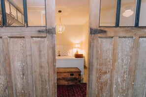A wooden door opening to a bedroom with a bed, a nightstand, a lamp, and a patterned carpet. - Vineyard Retreat | Artsy Charm, Deck & Guest Suite (Oak Bluffs)