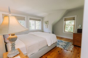 Une chambre à coucher avec un lit, une lampe, une commode et deux fenêtres avec des rideaux.