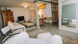 Ein Wohnzimmer mit Sofa, Fernseher, Schrank und Schreibtisch mit Lampe.