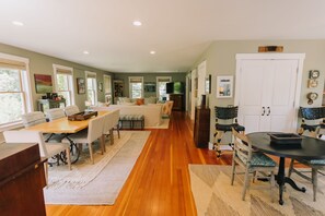 A spacious living area with a dining table, sofas, and a kitchen in the background. - Vineyard Retreat | Artsy Charm, Deck & Guest Suite (Oak Bluffs)