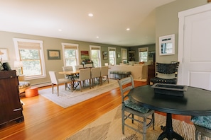 A spacious living area with a dining table, chairs, and a large window. - Artsy Vineyard Escape w/ Deck & Guest Suite (Oak Bluffs)