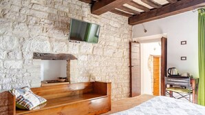 Una habitación rústica con pared de piedra, banca de madera, cama y televisor montado en la pared.