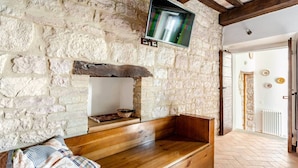 Una pared de piedra rústica con un banco de madera, un televisor montado y una puerta que da a otra habitación.