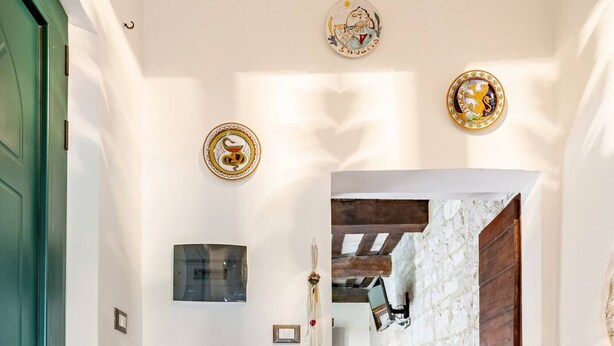 Un pasillo con una puerta verde, un muro de piedra y una puerta de madera que da a otra habitación.