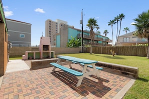 Eine Terrassenfläche mit Picknicktisch und Grill, umgeben von Pflaster und Holzzaun.