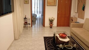 A living room with a sofa, a coffee table with a decorative bowl, a small side table, a door, and a hallway leading to another room. - ANNA LITTLE HOUSE Vacation Home (Bari)
