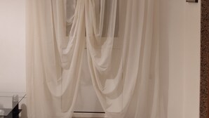 A room with a large window covered by sheer curtains, a framed picture on the wall, and a small table with a bottle. - ANNA LITTLE HOUSE Vacation Home (Bari)